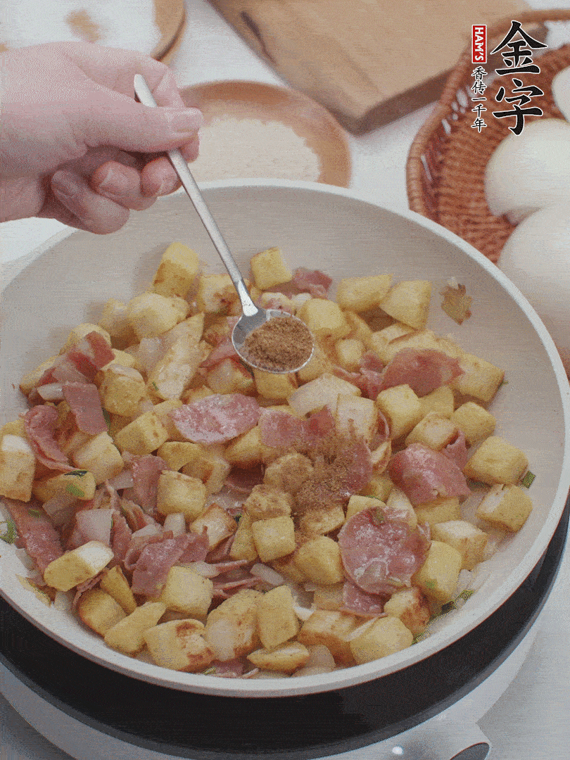 起鍋少油，煸香洋蔥丁、蔥白，加入金字培根火腿翻炒幾下，再加入饅頭丁、1小勺孜然粉、少許鹽翻炒均勻并鋪平。